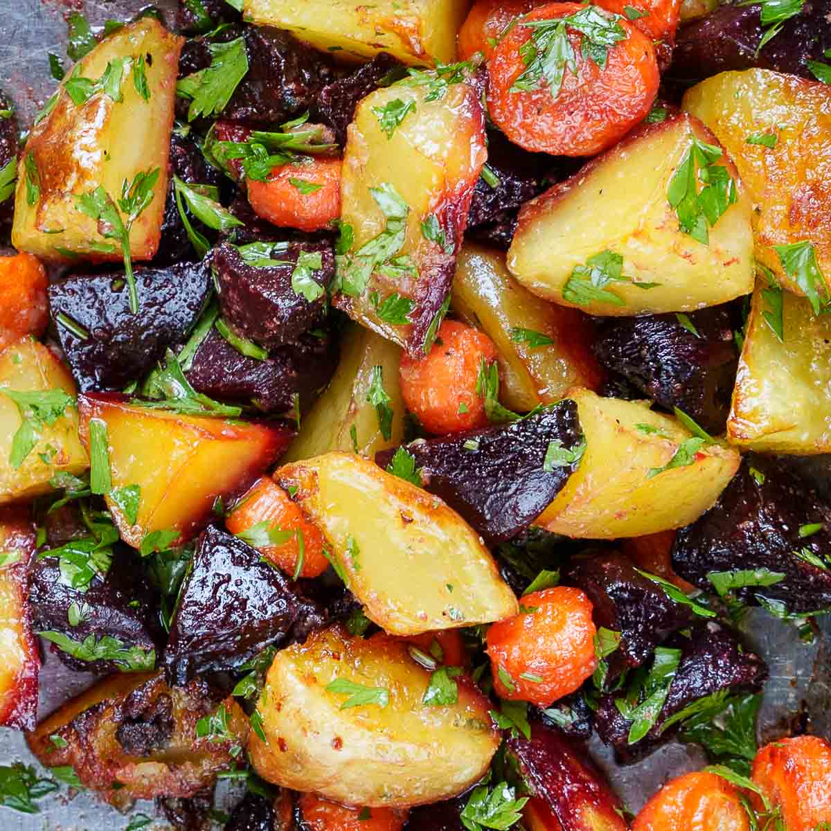 Nærbilde av ovnsbakte grønnsaker med dressing og bladpersille, sett ovenfra.