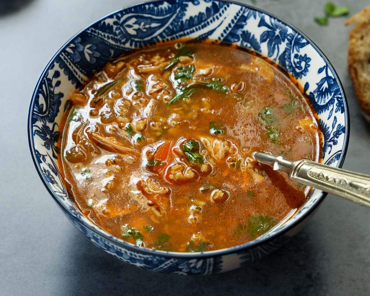 Nærbilde av kyllingsuppe med frikeh i blåmønstret bolle på mørk bakgrunn, sett fra øyenivå