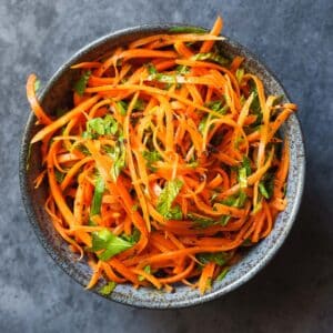 Gulrotsalat med urter i skål på mørk bakgrunn, sett ovenfra