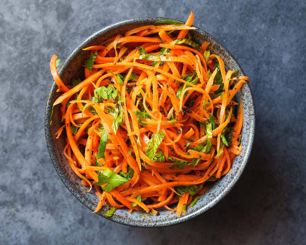 Gulrotsalat med urter i skål på mørk bakgrunn, sett ovenfra