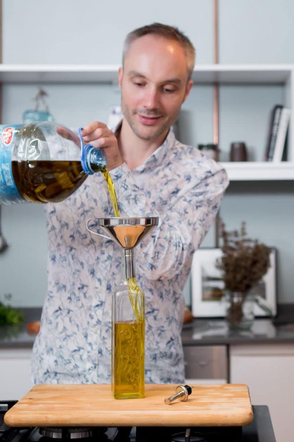 Vidar Bergum heller olivenolje fra en 5-litersdunk over i en liten glassflaske.